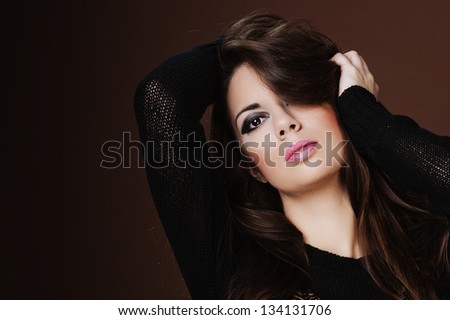 Woman leaning against brown background with hand in hair