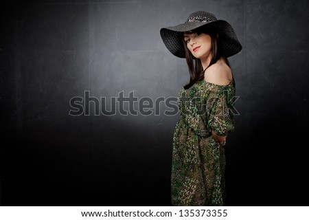 A woman saw in the gauzy dress and with hat on the dark background