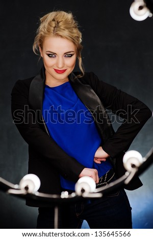 Young beautiful blonde on the dark background in the light of lamps/ Businesswoman posing in front of lightings of the theatre