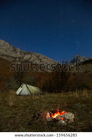 Campfire and tent in the mountains. Night, moonlight and stars