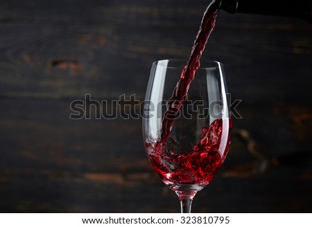 Pouring red wine into the glass against dark wooden background