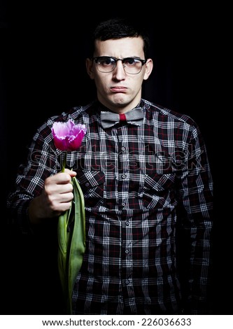 Close-up of an attractive young man in shirt bow tie and glasses holding a tulip.