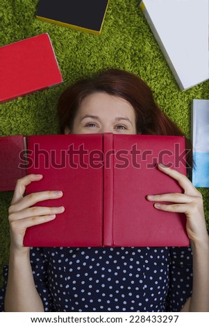Women portrait lying down on artificial green grass covering her face with a red journal, notebook