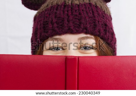 Close up of young woman holding red  book or diary wearing a winter hat looking like a head bear isolated on white background.