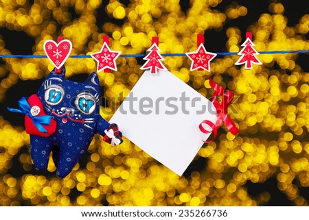 Christmas decoration  and a cat toy and empty sheet of paper with a red ribbon hanging on rope over golden blurred lights background