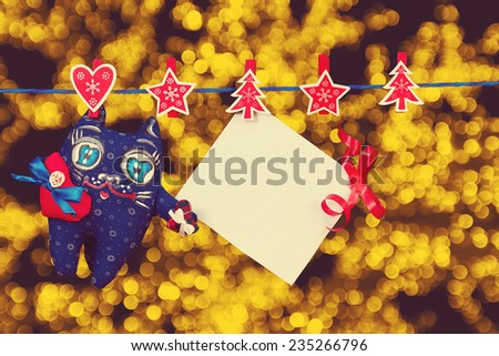 Christmas decoration  and a cat toy and empty sheet of paper with a red ribbon hanging on rope over golden blurred lights background