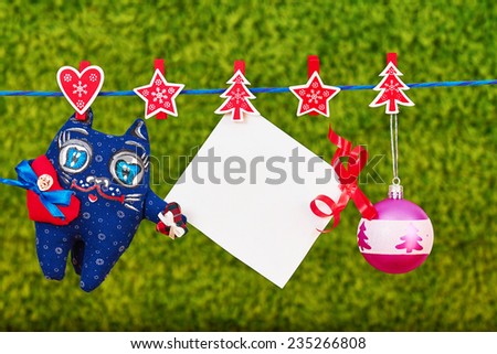 Christmas decoration  and a cat toy and empty sheet of paper with a red ribbon hanging on rope over green background