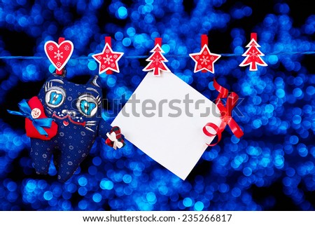 Christmas decoration and a cat toy and empty sheet of paper with a red ribbon hanging on rope over golden blurred lights background