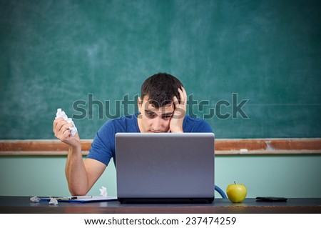 Stressed overworked man studying in front of notebook holding a paper in hand thinking to start from the beginning again isolated on a blackboard background.Facial expression.Idea.