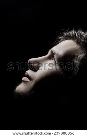 Portrait of a student,man side profile looking up lighted on a half face isolated on black background.Concept hope,freedom,.Face expression.