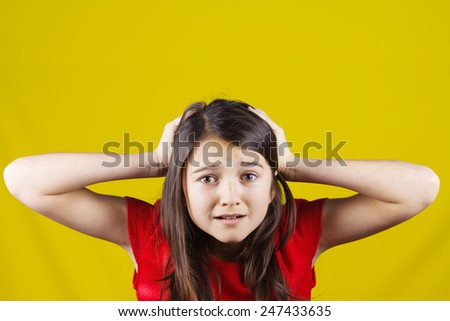 Stressed,depressed,unhappy little girl holding hands on her head over yellow background.