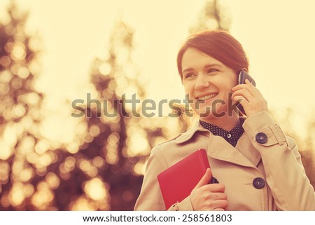 Young smiling businesswoman,student professional outdoors talking on cell smart phone and  holding a red journal.Businesswoman smiling,Life style,