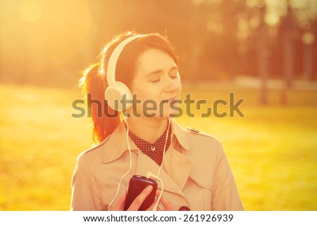 Woman listening to music in headphones in park  in sunlight in a sunny day. Young smiling businesswoman,student ,professional outdoors listening to music. Businesswoman smiling,Life style,