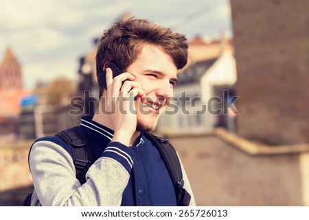 Smiling young man talking on mobile phone in a city .Young smiling student  outdoors talking on cell smart phone.Life style.City