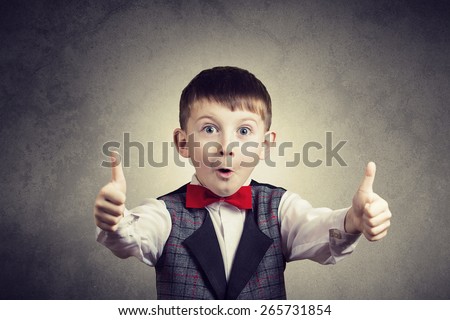 Excited Surprised  little boy with thumb up gesture isolated over grey background.