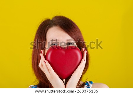 Woman showing holding  red heart. Love  concept with joyful young woman smiling isolated on yellow  background.