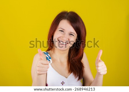 Happy surprised  young  woman very excited holding thumbs up isolated on yellow background.