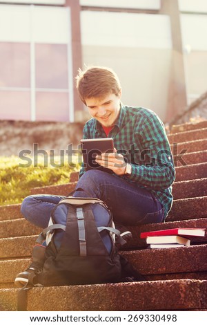Smiling young man taping on tablet in a city on stair .Young smiling student  outdoors  with tablet.Life style.City