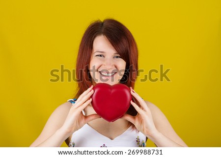 Woman showing holding red heart. Love  concept with joyful young woman smiling isolated on yellow  background.