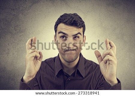 Portrait of Young man,student wishing something hardly,very much with crossed fingers over grey background.Praying for something very hardly,very much.