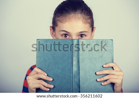 Little girl hiding herself behind book, studying, loving to learn.Cute little girl  hiding behind a book, isolated over white.