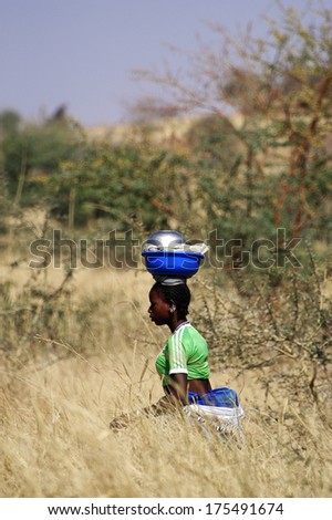 KOUPELA, BURKINA FASO - JANUARY 13: the African women carrying heavy loads sometimes on their heads over long distances through the bush, january 13, 2008.