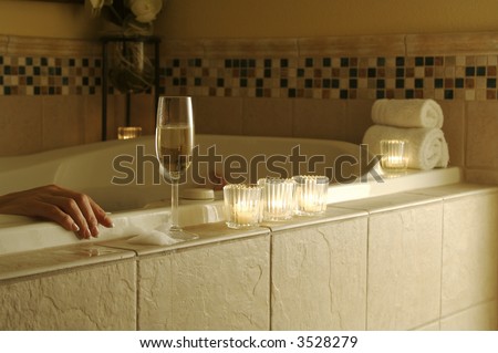 Woman relaxing in a tiled tub. Sparkling wine, candles and towels adorn the scene.