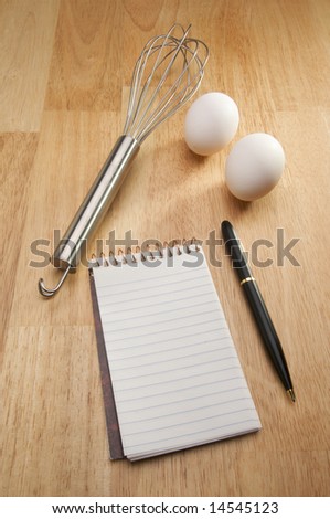 Mixer, Eggs, Pen and Pad of Paper on a wood background.