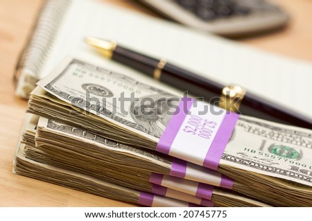 Stack of Money, Calculator, Pad of Paper and Pen with Narrow Depth of Field.