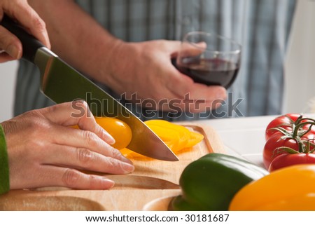 Woman Slicing Vegetables on Cutting Board While Man Enjoys a Glass of Red Wine.