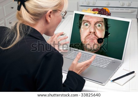 Shocked Woman In Kitchen Using Laptop with Grumpy Customer Support Man On Screen. Screen image can easily be replaced using the included clipping path.