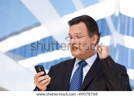 Excited Businessman Looking at Cell Phone Clinches His Fist in Joy Outside of Corporate Building.