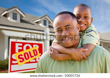 Happy African American Father and Son in Front of New Home and Sold Real Estate Sign.