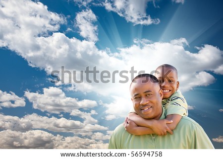 Happy African American Man with Child Over Blue Sky, Clouds and Sun Rays.
