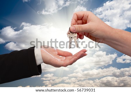 Male Hand Handing Over Keys to Female Hand On Dramatic Clouds and Sun Rays.