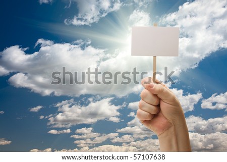 Man Holding Blank Sign Over Dramatic Clouds and Blue Sky with Sun Rays - Ready For Your Own Message on Sign and Over Clouds.