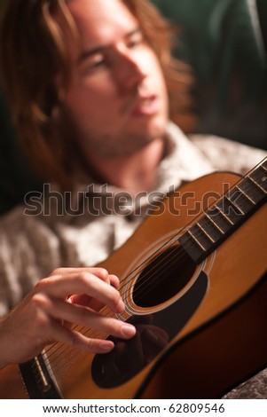 Young Musician Plays His Acoustic Guitar under Dramatic Lighting.