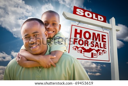 Happy African American Father with Son In Front of Sold Home For Sale Real Estate Sign and Sky.