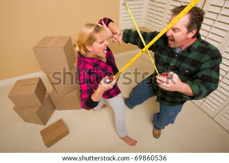 Couple Having a Fun Sword Fight with Their Tape Measures Surrounded by Packed Moving Boxes.