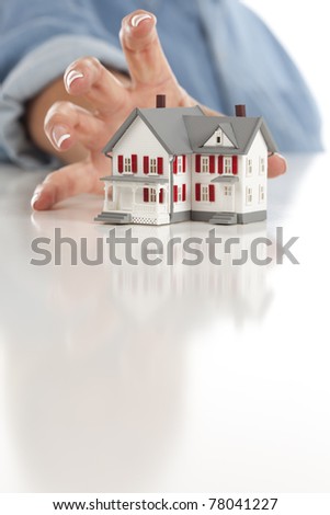 Woman's Hand Reaching for Model House on a White Surface.