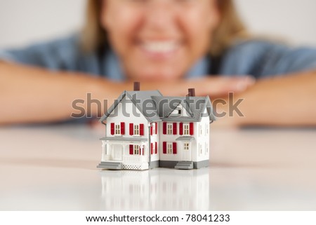 Smiling Woman Leaning on Hands Behind Model House on a White Surface.