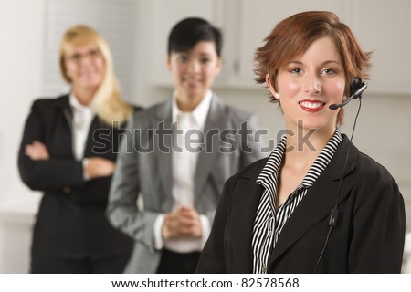 Pretty Red Haired Businesswoman with Headset and Colleagues Behind in Office Setting.