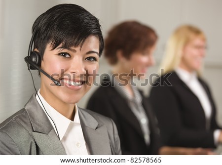 Pretty Hispanic Businesswoman with Colleagues Behind in an Office Setting.