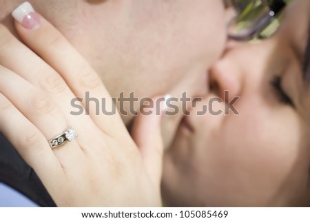 Young Female Hand with Engagement Ring Touching Fiance's Face as They Kiss with Selective Focus on the Ring.