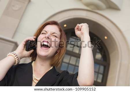 Young Businesswoman with Fist in the Air On Cell Phone in Front of Building.