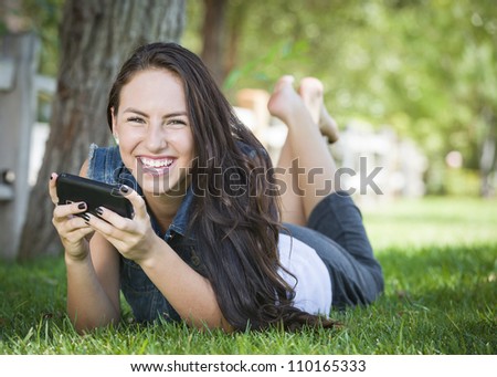 Attractive Happy Mixed Race Young Female Texting on Her Cell Phone Outside Laying in the Grass.
