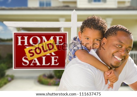 Happy Mixed Race Father and Son In Front of Sold Real Estate Sign and New House.