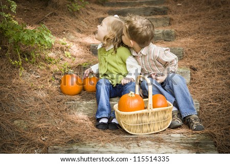 Adorable Brother and Sister Children Sitting on Wood Steps with Pumpkins Whispering Secrets or Trying to Kiss Cheek.