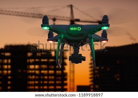 Silhouette of Unmanned Aircraft System (UAV) Quadcopter Drone In The Air Over Buildings Under Construction.