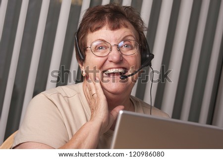 Smiling Senior Adult Woman with Telephone Headset In Front of Computer Monitor.